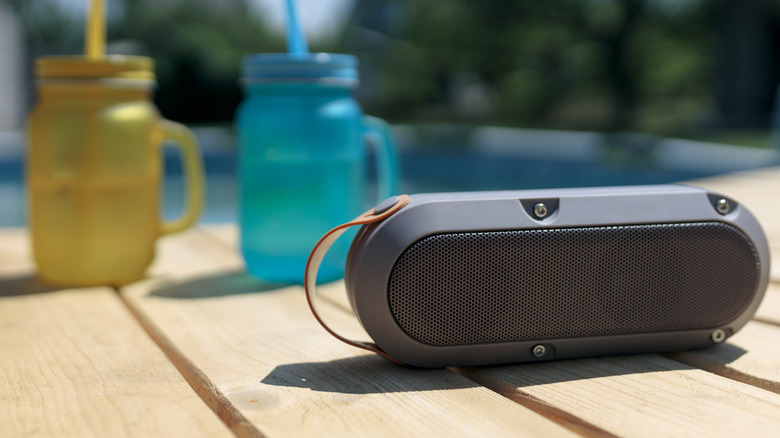 A Bluetooth speaker next to two beakers, on the side of a pool.