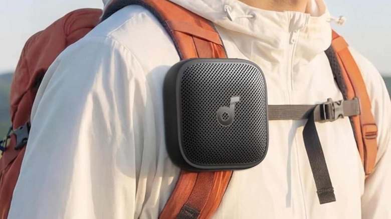 The Soundcore Boom Go 3i attached to a backpack strap, worn by a hiker.