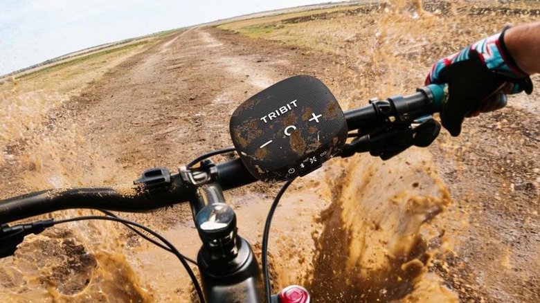 The Tribit Stormbox Micro 3 on a bike handlebar as it gets splashed with muddy water.