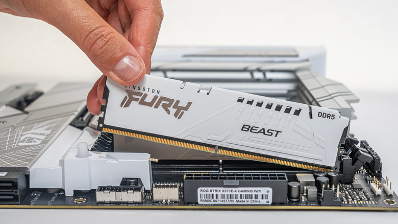 A hand installs a white DDR5 memory module in a motherboard.