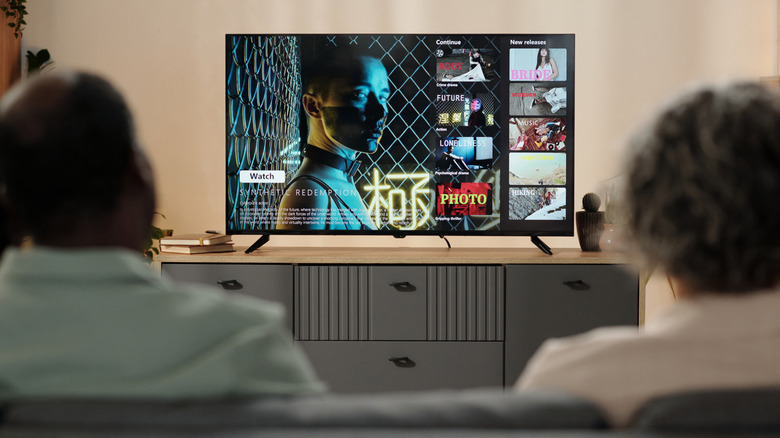 Two people watching a flat-screen TV featuring the title card of a show in a living room setting