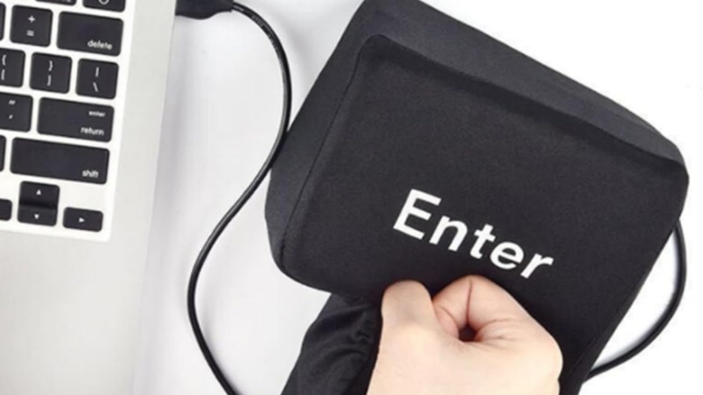 Man hitting large black enter key pillow placed next to a laptop