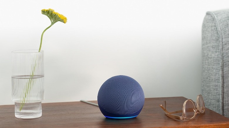 Blue Echo Dot placed beside a vase and glasses on a wooden table.