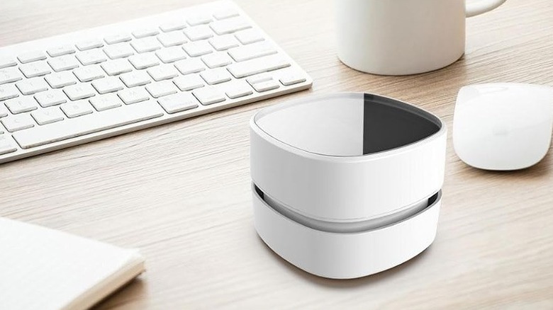 Portable vacuum cleaner placed on a desk alongside keyboard, mouse and a mug.