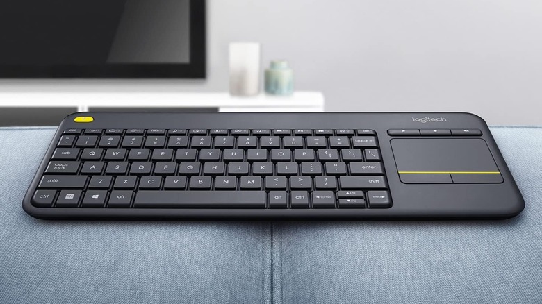 A media keyboard rests on a couch with a TV visible in the background.