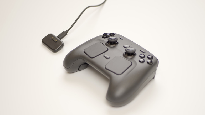 A Valve Steam controller next to its charging puck.