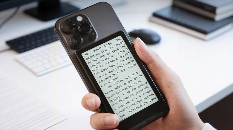 A hand holding an iPhone with XTEINK X4 e-reader magnetically attached to the rear side