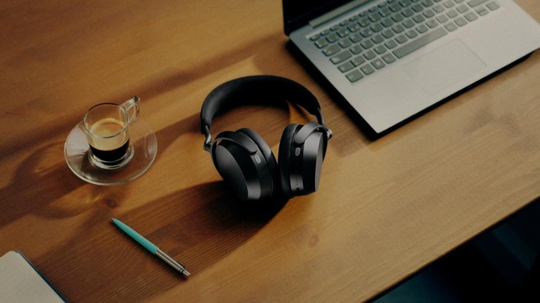 A pair of the new Sennheiser Momemntum 5 headphones on a desk next to a laptop, pen, and cup of water