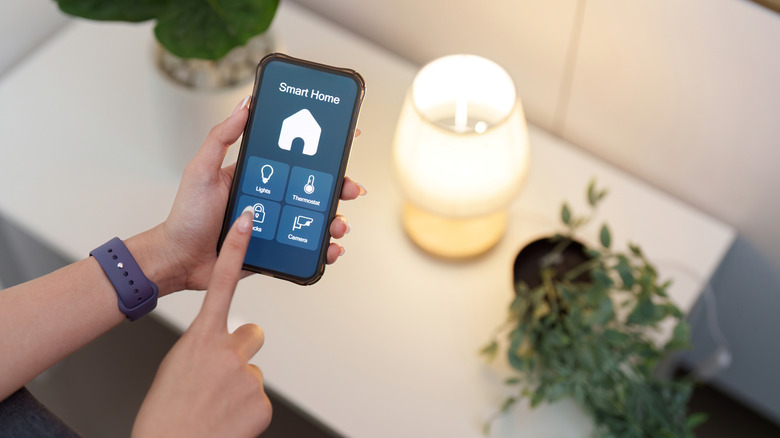 A smart home app open on a person's phone, near a table with two plants and a lamp