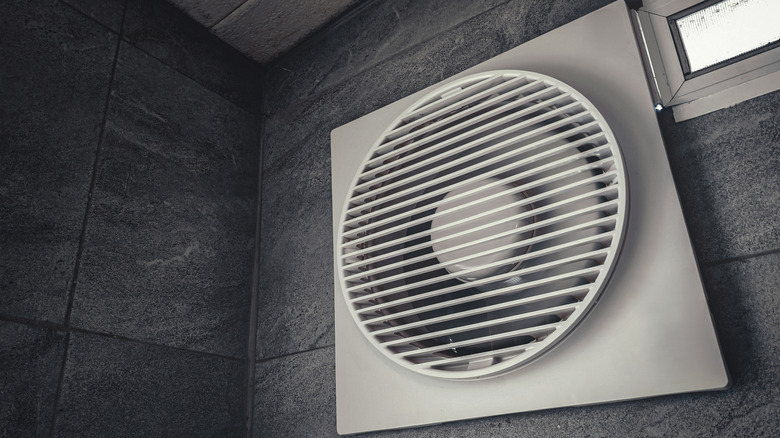 An exhaust fan installed on a wall with gray tiles