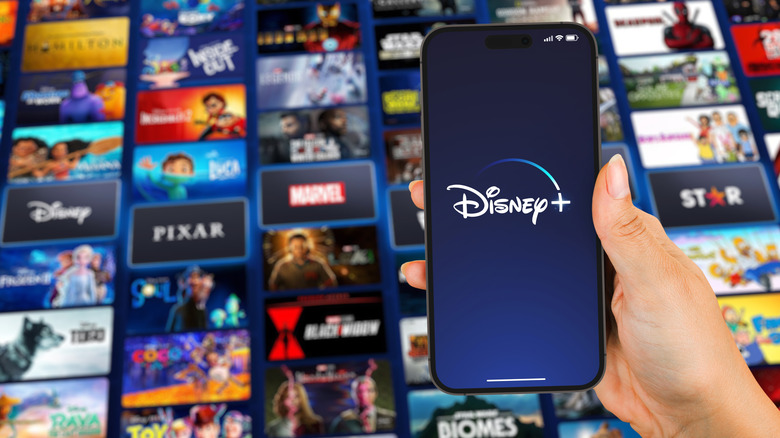 A person holding a phone with the Disney logo, with a bunch of Disney movies in the background