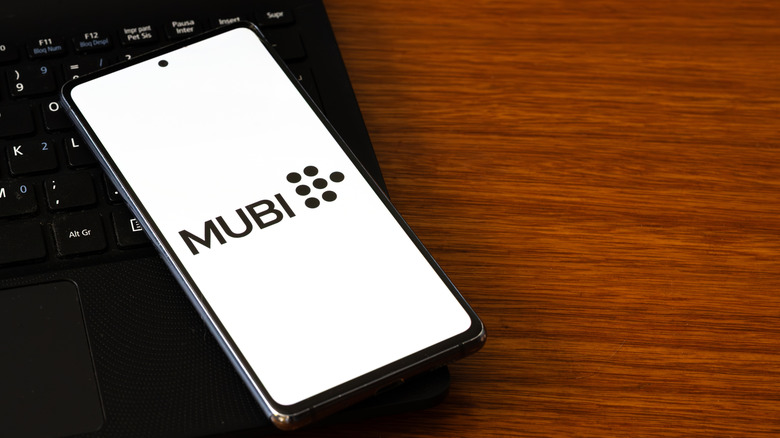 A smartpphone lying on a laptop, showing the Mubi logo on a white background