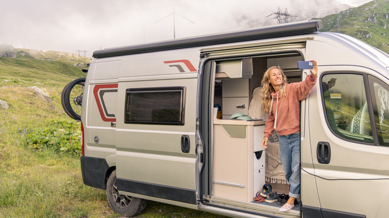 A woman standing inside her RV camper van taking a photo with her iPhone.