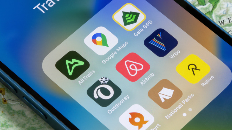 A picture of an iPhone showing a Travel folder with apps such as AllTrails, Google Maps, Outdoorsy, The Dyrt, National Parks, etc.