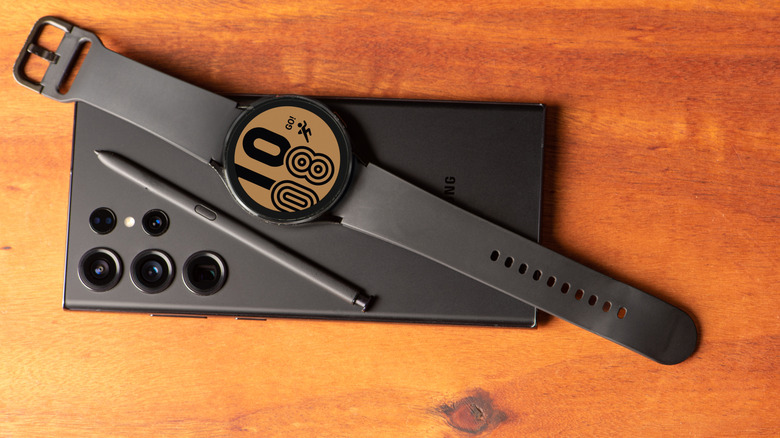 A Samsung Galaxy Watch and S-Pen laid on top of a Galaxy S23 Ultra on a wooden table.