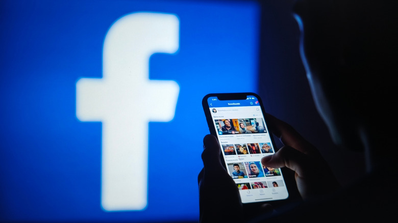 A person using Facebook in front of the company logo