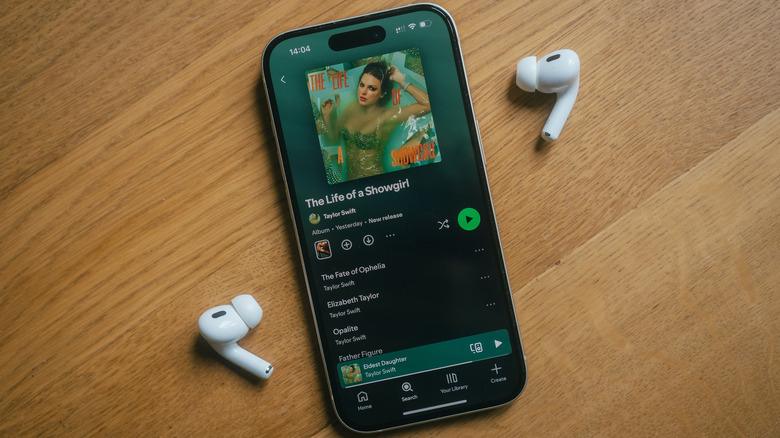 "The Life of a Showgirl," Taylor Swift's album, open on Spotify on a smartphone, placed on a wooden surface next to some wireless earbuds