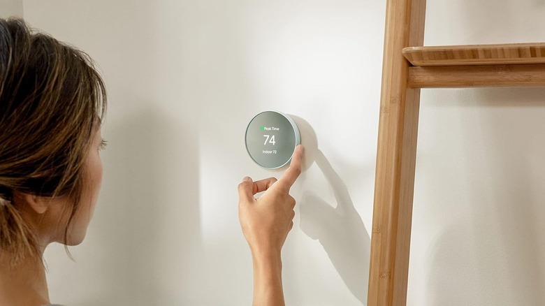 A woman is adjusting her Google Nest home thermostat on a cream colored wall