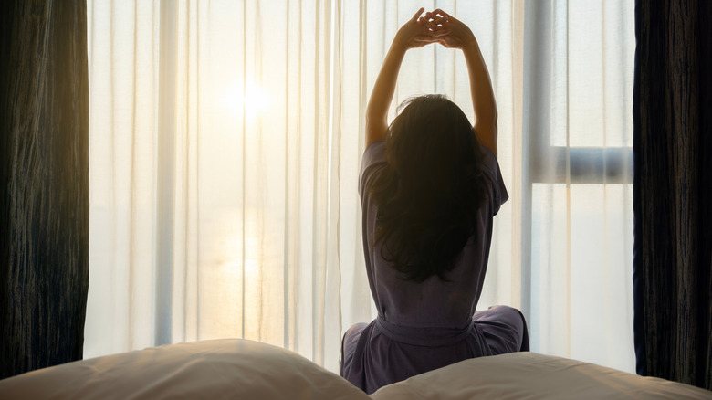 A woman stretches in the bed as sunshines on her from the big window