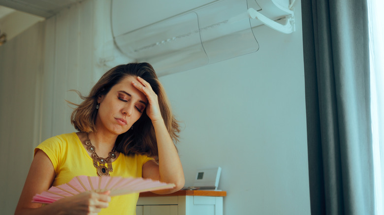 Woman Using a Hand Fan Having a Broken Air Conditioning Machine
