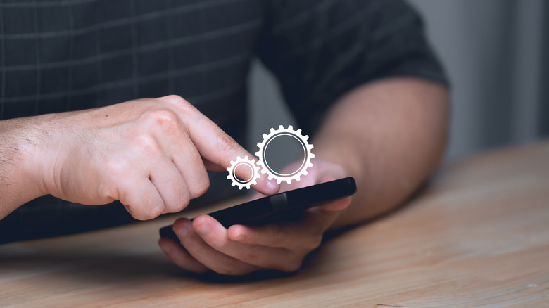 A person tapping a smartphone screen with a settings icon in view