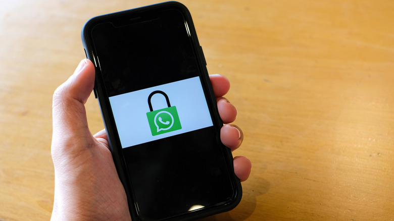 A person holding a smartphone showing the WhatsApp logo inside a padlock icon