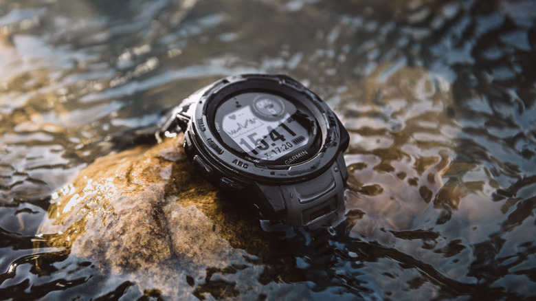 A Garmin Instinct watch on top of a rock in water