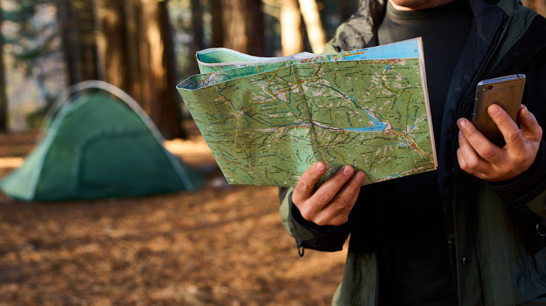 Camper holding a phone and a map outside a green tent