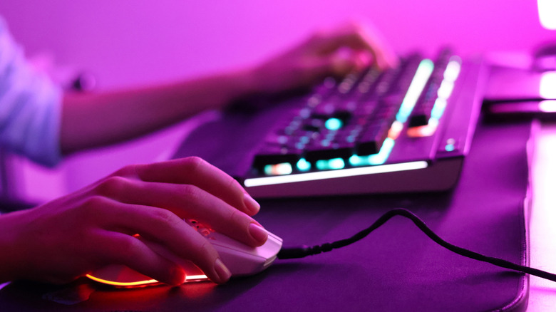 A person using a wired mouse and keyboard on their desk, both of which are backlit