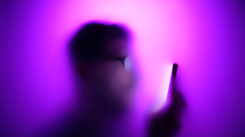 A man behind a purple and white glass looking into a smartphone.