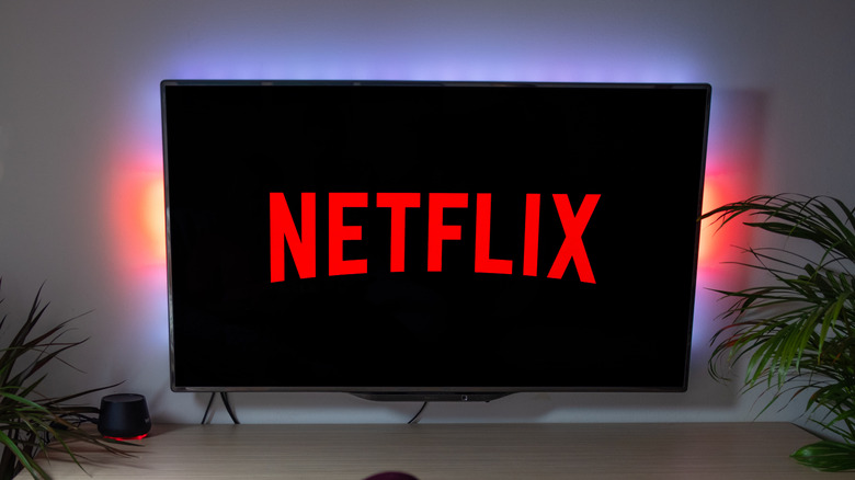 Woman with popcorn holding a remote control, watching a TV screen displaying the Netflix logo.