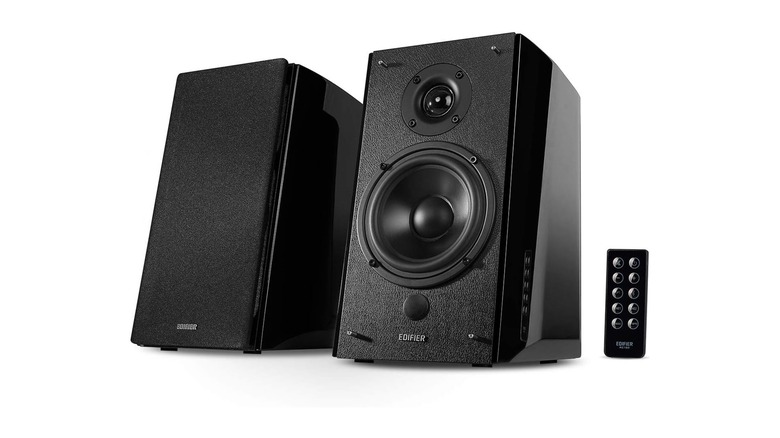 Two black bookshelf speakers, placed vertically, next to a remote