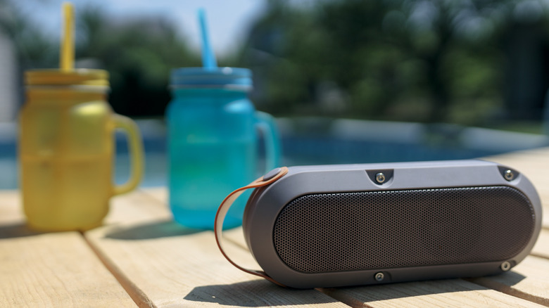 A Bluetooth speaker with a pair of water bottles beside a pool.