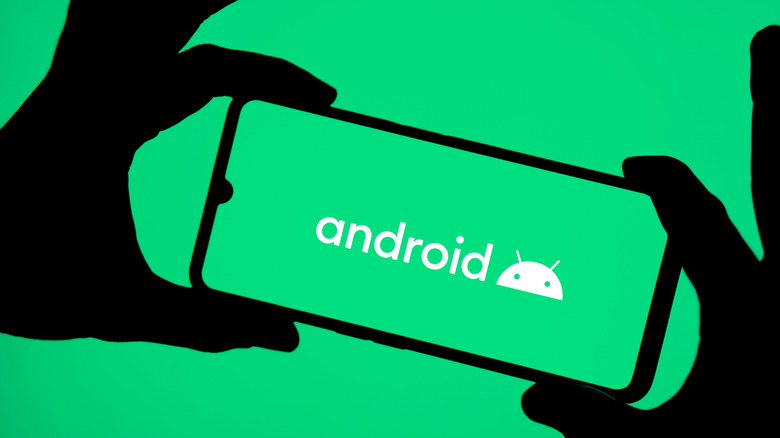 A phone being held by two hands showing the Android logo on the screen