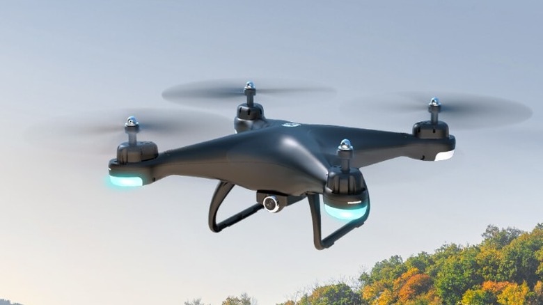 Holy Stone HS110D hovering in the air with a forest in the background.