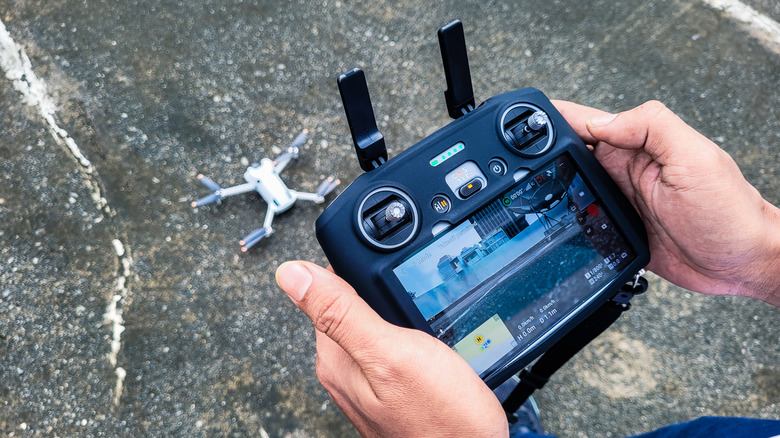 Closeup of a person handling the controller of a drone, with the drone in the background.