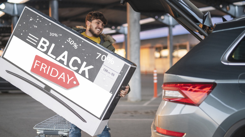 A young happy man loading a brand new TV at Black Friday sale