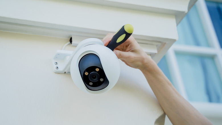 An outdoor security camera being installed by a person holding a screwdriver.