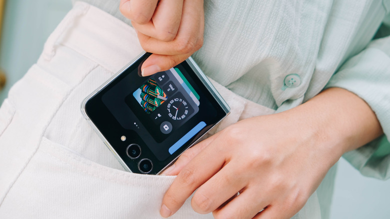 A person putting a clamshell folding phone in their pocket