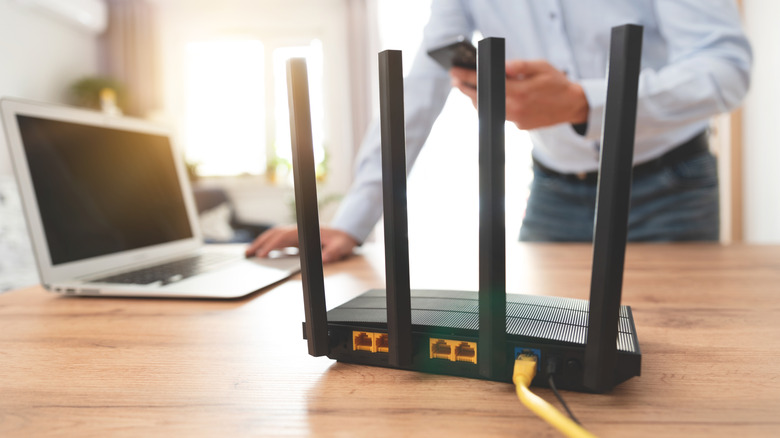 A router in the foreground with a person operating a laptop blurred in the background.