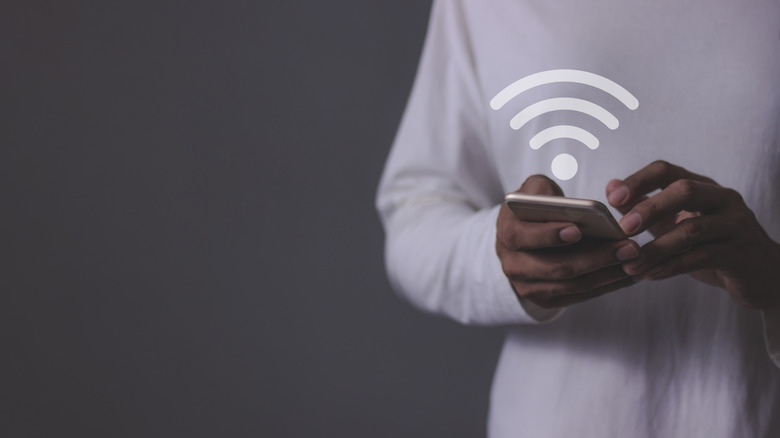 A person holding a smartphone with a Wi-Fi symbol hovering above it.