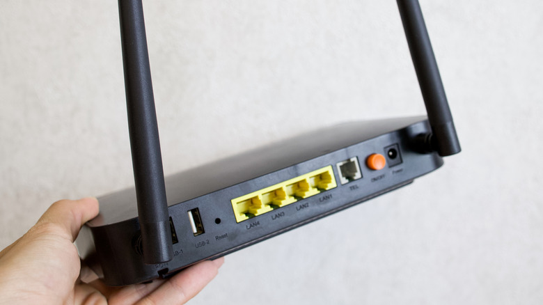 A hand holding a two-antenna black router with USB and Ethernet ports at the rear.
