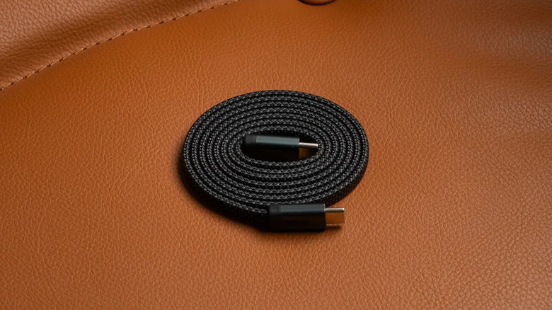 A black Statik USB-C magnetic cable coiled up and placed on a brown leather surface.