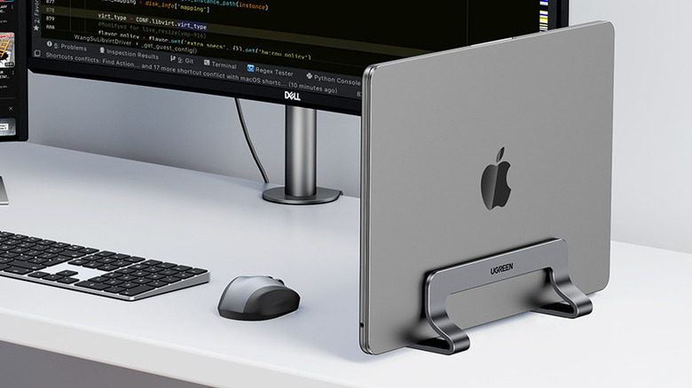 A MacBook placed on the UGREEN Vertical Laptop Stand on a white desk.
