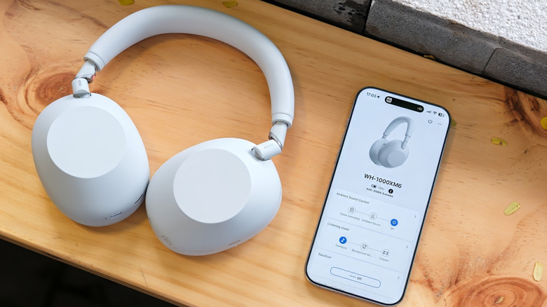A pair of white Sony WH-1000XM6 headphones next to an iPhone 16