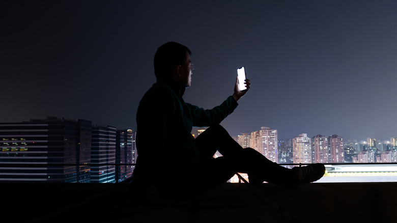 A person using a smartphone on the roof of a building at night