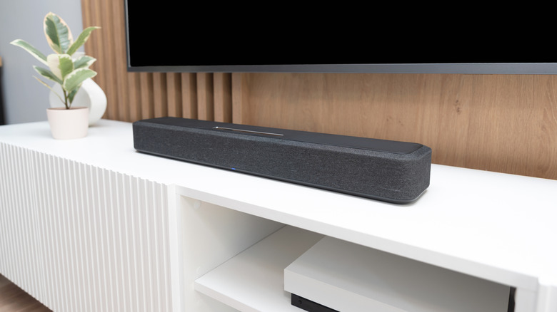 A dark gray soundbar placed under a TV atop a white media console.