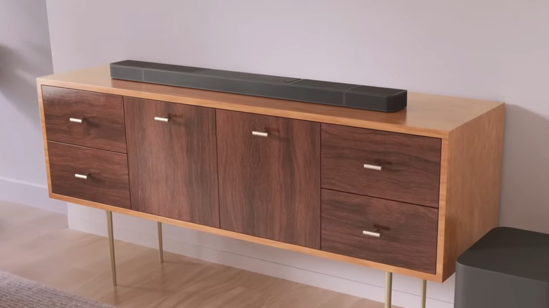 A black JBL Bar 1300X soundbar atop a wooden media console with the included subwoofer at the console's right.