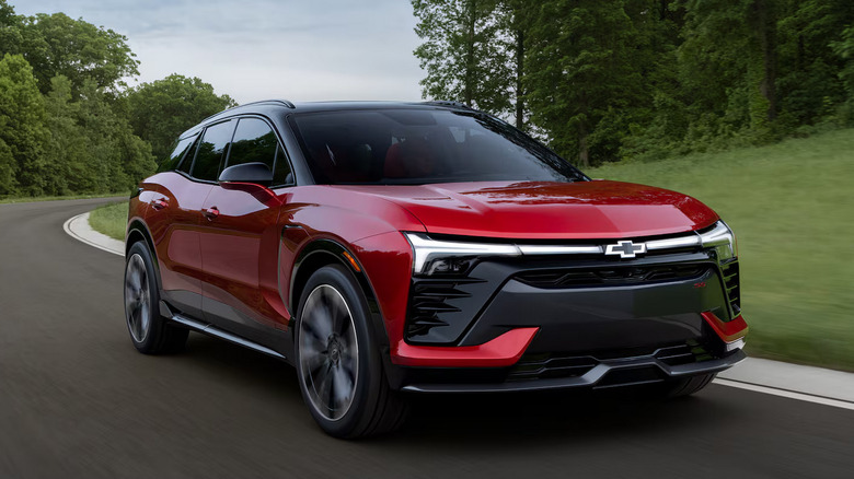 A red Chevrolet Blazer EV driving down a road surrounded by trees