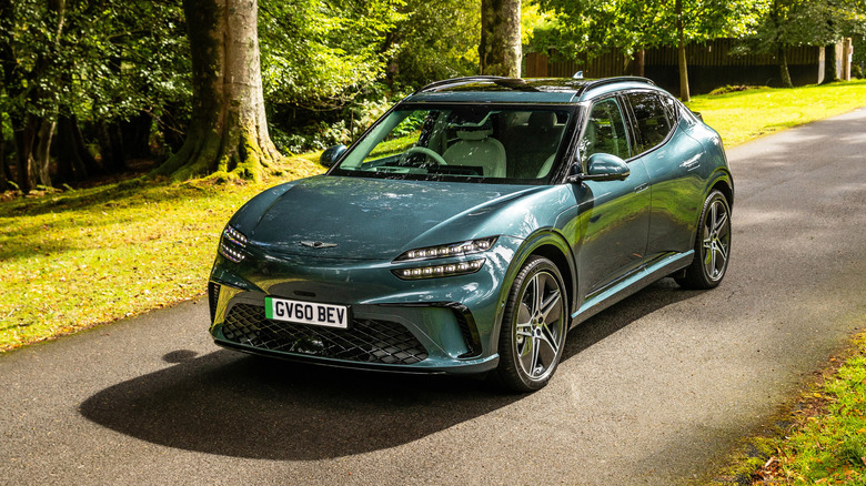A green Genesis GV60 parked on a road surrounded by trees
